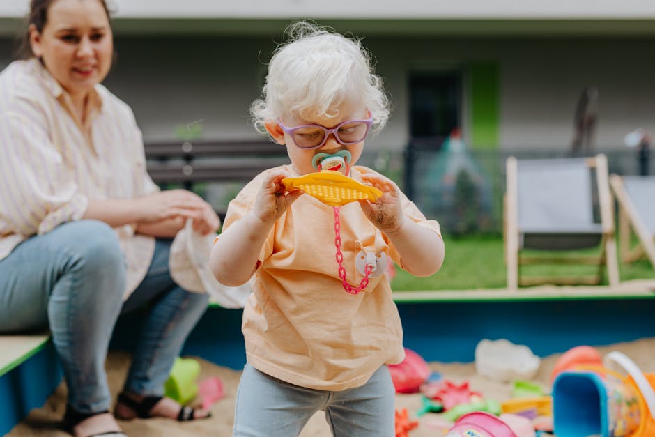 A young girl with glasses playing in a sandbox, exploring toys.