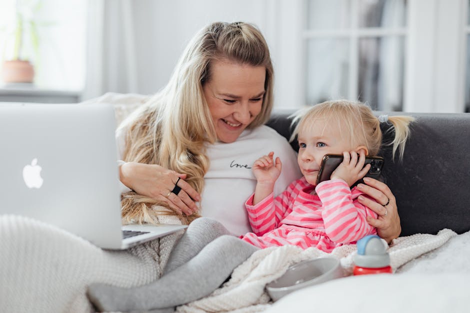 A joyful mother and daughter enjoy bonding time on a couch with a laptop and phone.