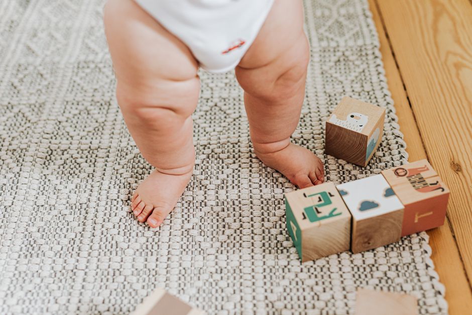 Capturing a baby's first steps with wooden building blocks on a soft indoor rug. Perfect for childhood memories.