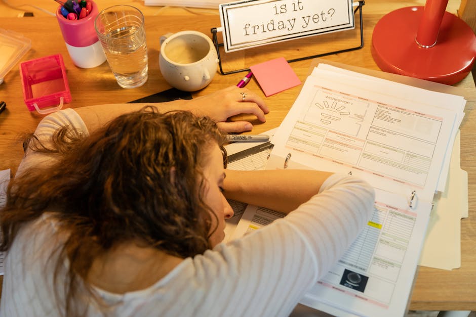 Woman sleeping at desk overwhelmed with work papers, showing fatigue.